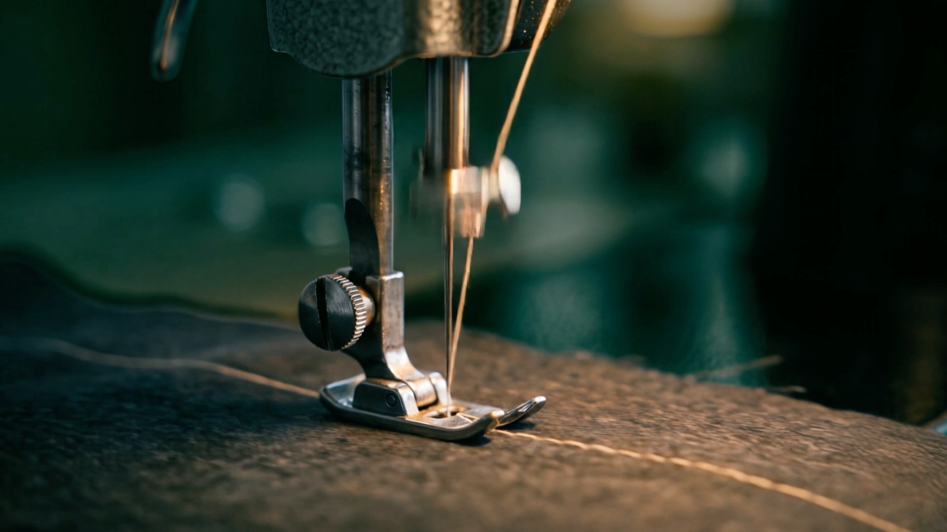 Needle of an industrial sewing machine stitching a seam through charcoal wool