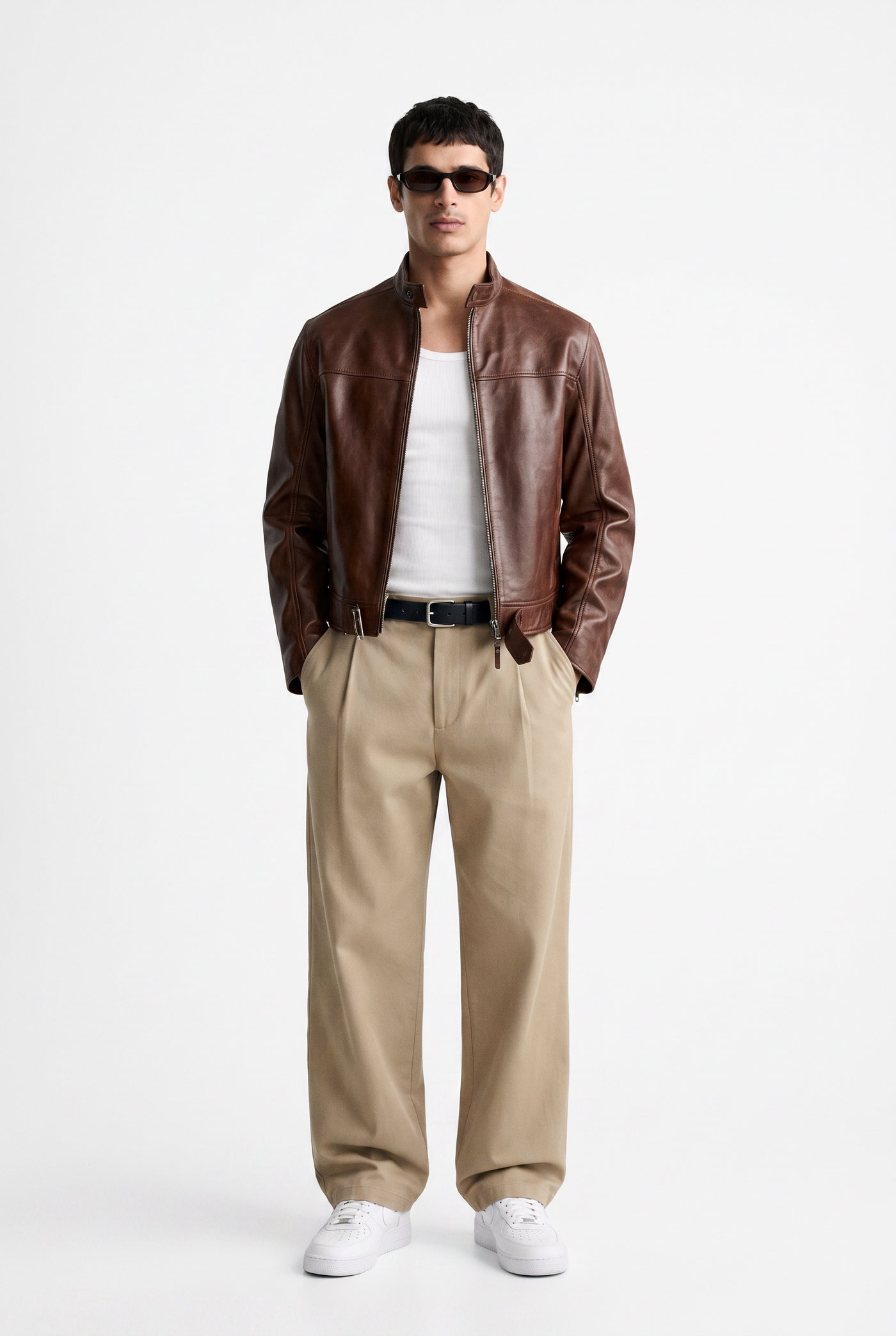 Man in a brown leather blouson over a white tee with tan pleated trousers
