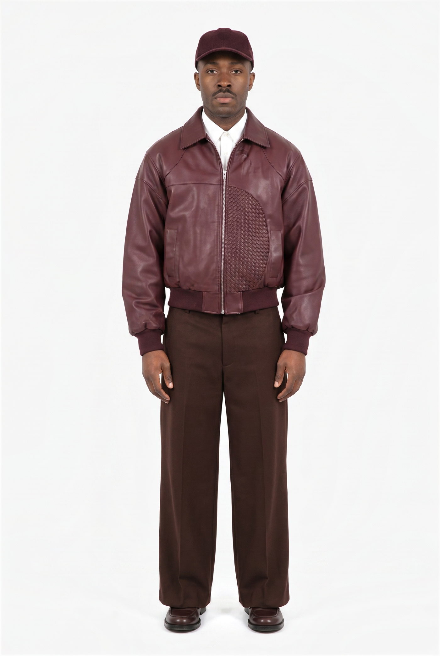 Man in a burgundy leather bomber, cap and brown wide leg trousers