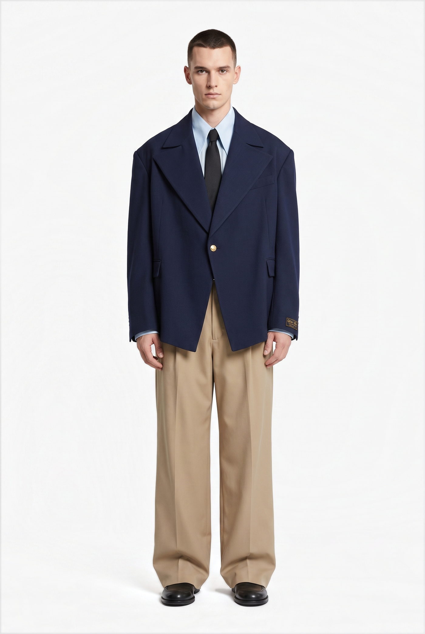 Man in a navy blazer over a blue shirt, tie and tan pleated trousers